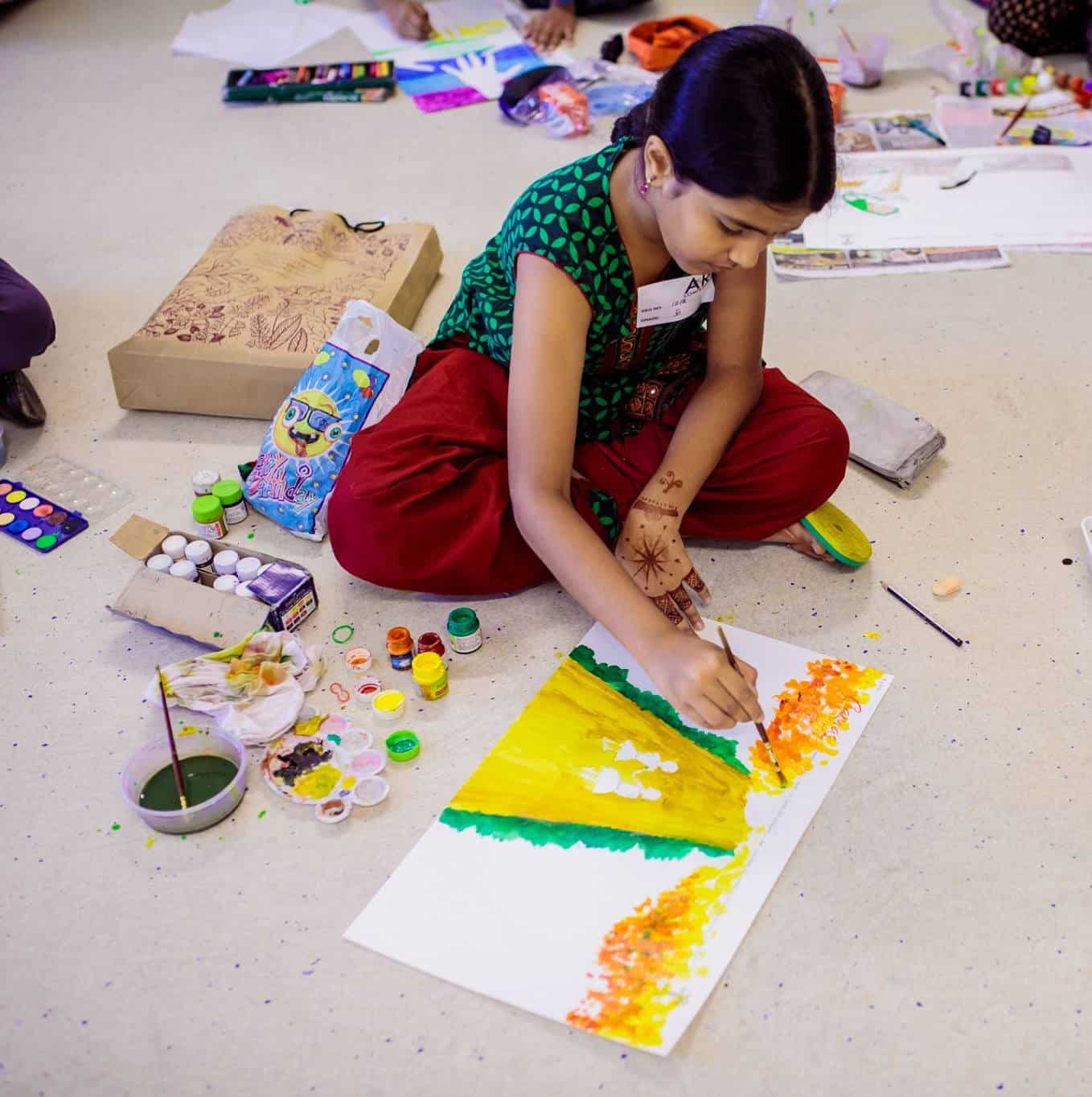Girl wearing green colour dress painting on a white colour chart using brush and paints